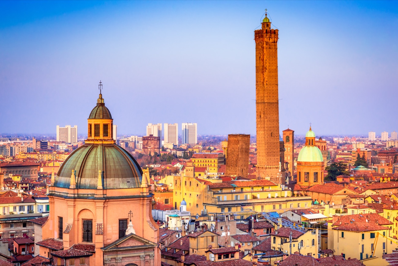 A copper church dome and the Asinelli Tower above the red rooftops of Bologna